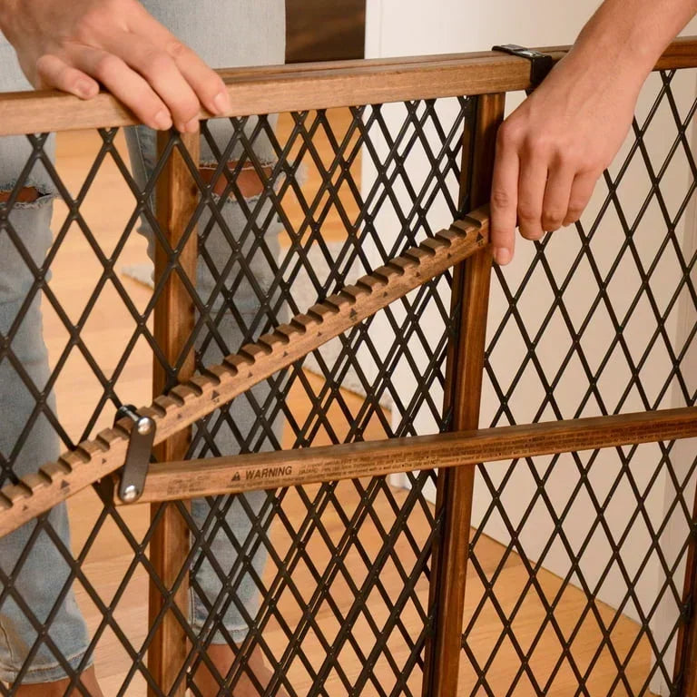 Hands adjusting wooden and metal baby safety gate with diamond-pattern mesh in home setting