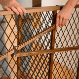 Hands adjusting wooden and metal baby safety gate with diamond-pattern mesh in home setting