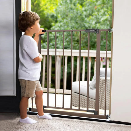 Toddler boy in white shirt and shorts standing by a brown safety gate inside a home doorway