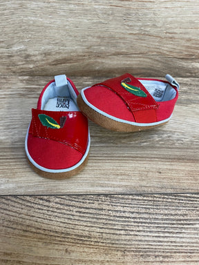 Front and side view of red TOMS Alpargata crib shoes showing embroidered green leaf on velcro strap and suede-like brown sole on wood background