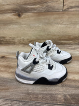 Three-quarter view of Air Jordan 4 Retro OG TD White Cement sneakers showing black accents and speckled gray midsoles on wood