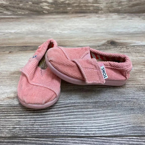 Three-quarter view of pink corduroy TOMS toddler slip-on shoes size 3C showing Velcro strap and rubber sole on wood background