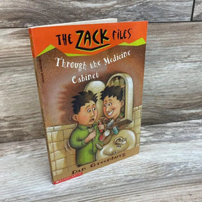 Three-quarter view of paperback Through the Medicine Cabinet (The Zack Files) showing illustrated front cover and spine on wood plank background