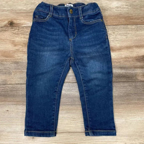 Flat lay of blue toddler skinny jeans (12–18m) showing elastic waistband, faux front pockets, and faded whiskering on wood backdrop