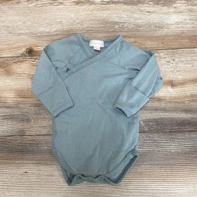 Flat lay of sage kimono bodysuit size 6-9 months with long sleeves, side wrap snaps and three bottom snaps on wood background