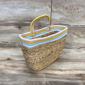 Three-quarter view of woven wall-hanging basket showcasing pastel pink, yellow, and blue coiled rope trim and handle on wooden background