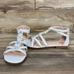 Side-front view of white Loganberry gladiator sandals, size 4Y, with iridescent flower T-strap and back zipper on wood