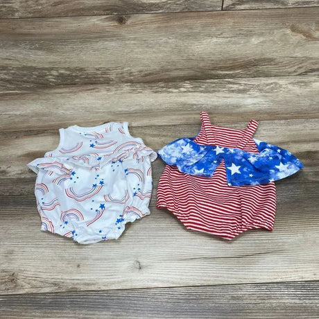 Top-down view of two newborn rompers: white rainbow-and-star romper and red striped romper with blue star ruffle on wood background