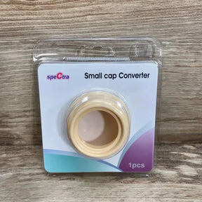 Front view of Spectra small cap converter, beige adapter in clear blister pack with label Small cap Converter on wood