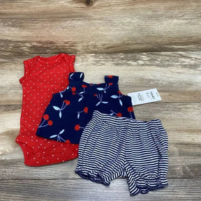 Flat lay newborn 3-piece set: red polka-dot bodysuit, navy cherry tank, navy-striped ruffle shorts on wood background