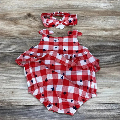 Flat lay of red and white gingham baby romper with navy stars and matching headband showcasing ruffle trim and front snaps with wood background