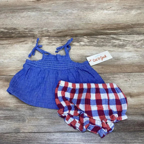 Flat lay of blue smocked top with red white blue gingham bloomers, tie straps and elastic ruffles on wood background