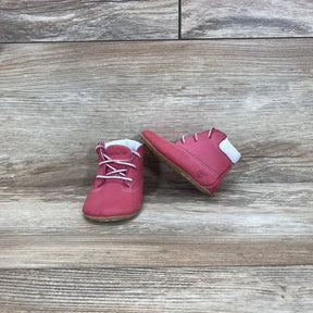 Front and side view of pink Timberland infant crib booties showing lace up leather upper, white collar, tan sole on wood
