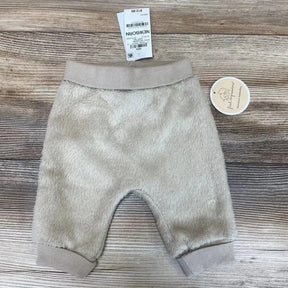 Top-down flat lay of tan newborn faux sherpa baby pants showing ribbed elastic waistband and cuffs on wood background