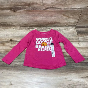 Flat lay of pink toddler long-sleeve shirt size 3T with text GRANDMA'S COOKIE BAKIN' HELPER and cookie graphic on wood floor
