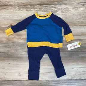 Flat lay of blue and navy waffle-knit baby shirt and pants set with yellow trim and shoulder snap on wood background