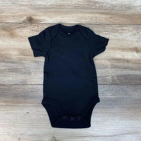 Flat lay of black newborn organic short-sleeve bodysuit with envelope shoulders and three snap crotch on wood background