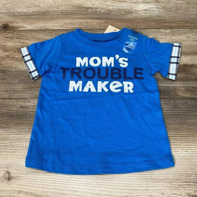 Flat lay of blue Mom's Trouble Maker baby T-shirt showcasing plaid sleeve cuffs and visible 6-9 months tag on wood background