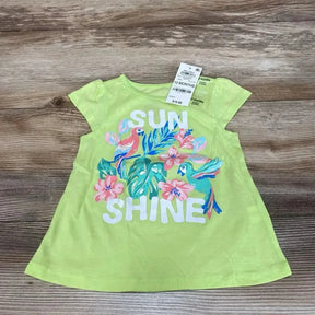Flat lay of lime green toddler T-shirt showing white SUN SHINE text and colorful tropical birds and flowers on wood table